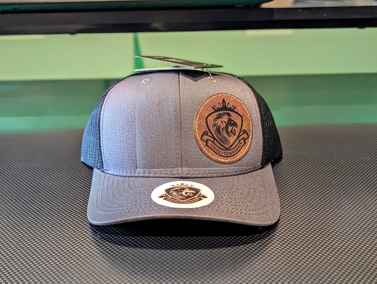 Gray and black trucker hat with a leather patch on a reflective surface