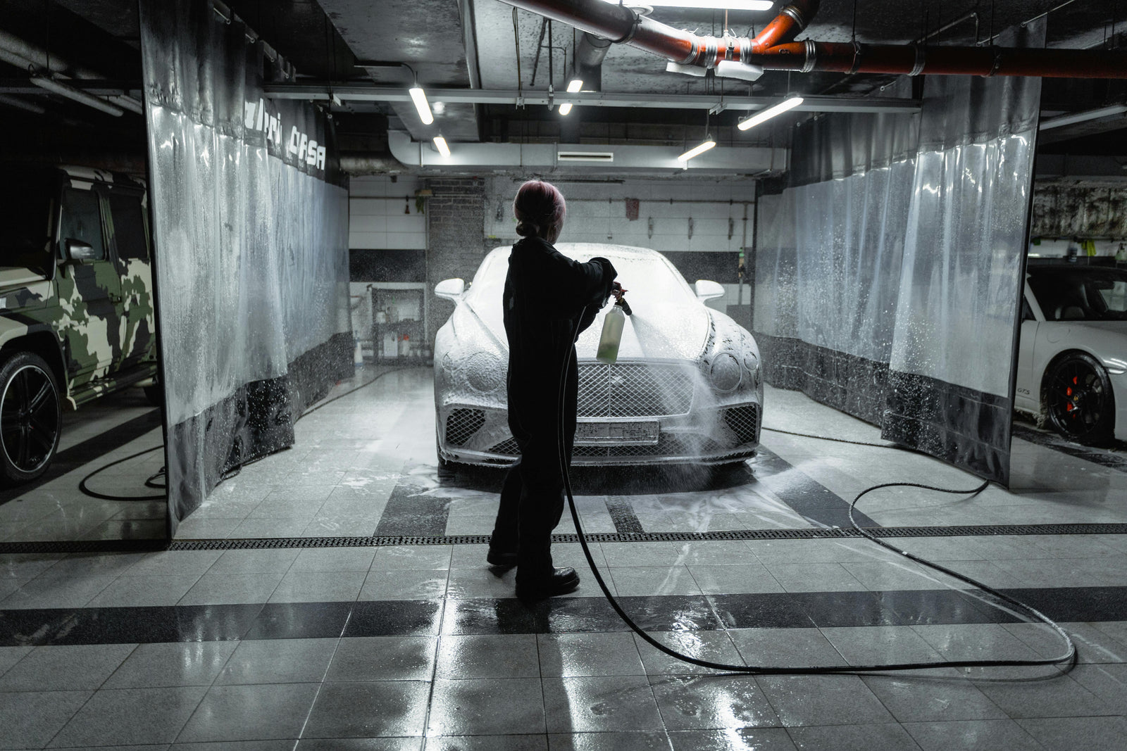 Person detailing luxury car with foam spray in modern garage, LynXautoinnovate automotive parts