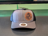 Gray and black trucker hat with a leather patch on a reflective surface