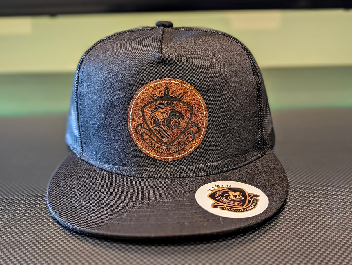 Black cap with brown leather patch featuring a logo on a textured surface