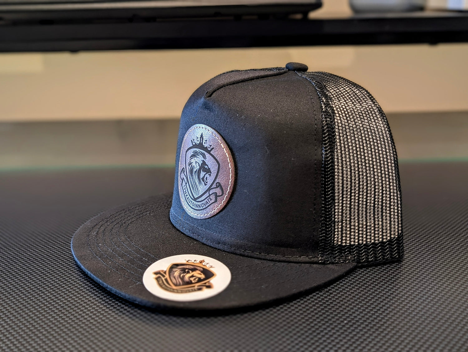 Black trucker cap with mesh back and embroidered logos on a textured surface