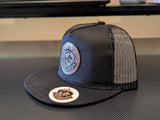 Black trucker cap with mesh back and embroidered logos on a textured surface