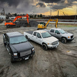 Three pickup trucks parked on a construction site with excavators in the background under a cloudy sky.